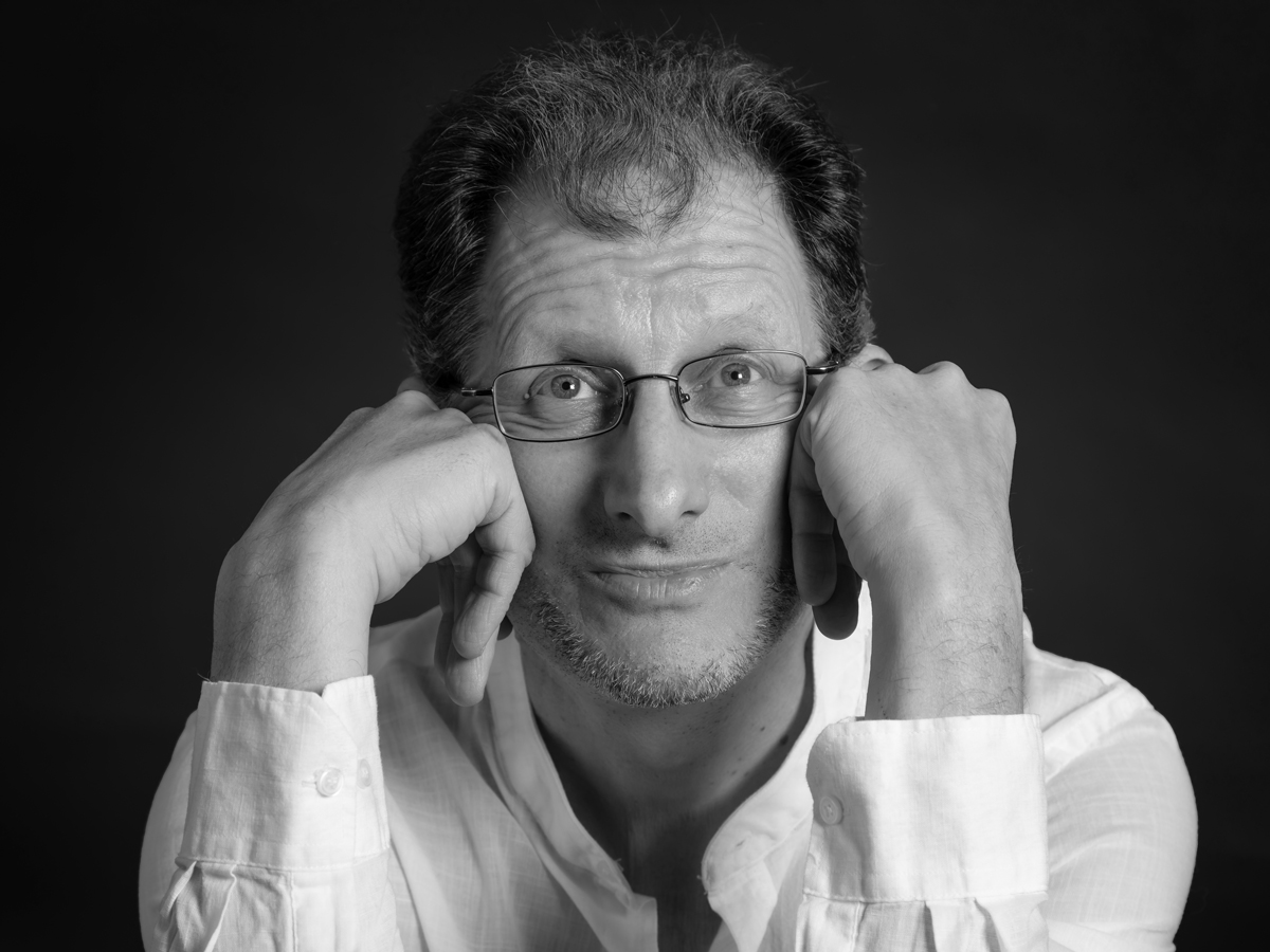 Schwarz-Weiss Aufnahme von Ivo Antognini. Dein Kopf in beide Hände gestützt, schaut er in die Kamera.